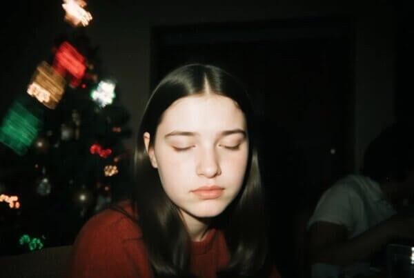 Gen Z young adult looking overwhelmed and isolated while sitting on a couch at a crowded family New Year's Eve party with blurred festive background.