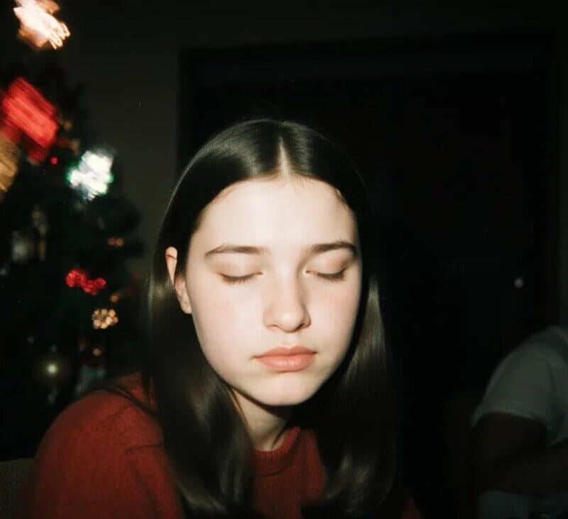Gen Z young adult looking overwhelmed and isolated while sitting on a couch at a crowded family New Year's Eve party with blurred festive background.