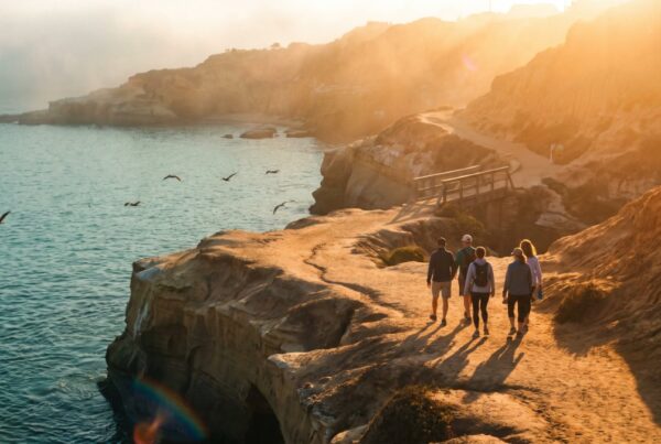 Adults walking a winding cliff path above La Jolla Cove at sunrise, the road ahead of an addiction aftercare program