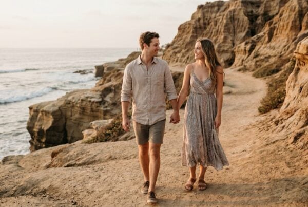 Young couple in casual beach clothing holding hands on a La Jolla coastal path at golden hour