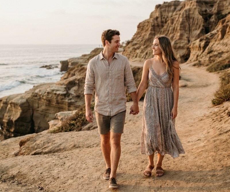 Young couple in casual beach clothing holding hands on a La Jolla coastal path at golden hour