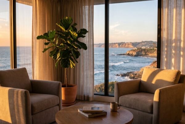 Sunlit therapy office with two armchairs facing an ocean-view window, rhythmic bands of light suggesting an EMDR session