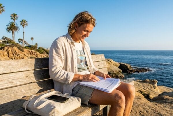 Young adult reviewing insurance paperwork on a bench overlooking La Jolla Cove in San Diego