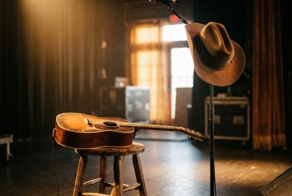Empty country stage with acoustic guitar and cowboy hat under a spotlight, evoking Morgan Wallen’s rehab story