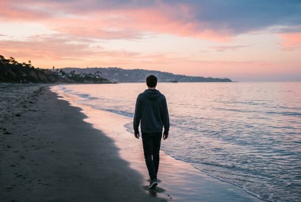 Young adult walking alone along La Jolla Shores at dawn, early sobriety and sleep